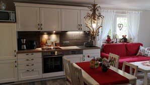Een keuken met witte kasten, een rode eettafel en een rode bank in de woonkamer.