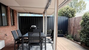 An outdoor patio with a table and chairs, a grill, and a brick wall. - JB’s - Jetty Busselton Stay (West Busselton)