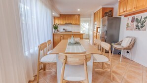 A modern kitchen with wooden cabinets, a dining table with chairs, and a refrigerator. - JB’s - Jetty Busselton Stay (West Busselton)