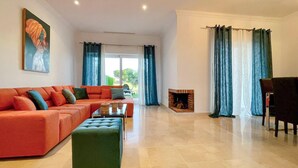 A spacious living room with a large orange sofa, a green ottoman, and a fireplace. - 2 bedroom nice home in Arcos de la Frontera (Arcos de la Frontera)