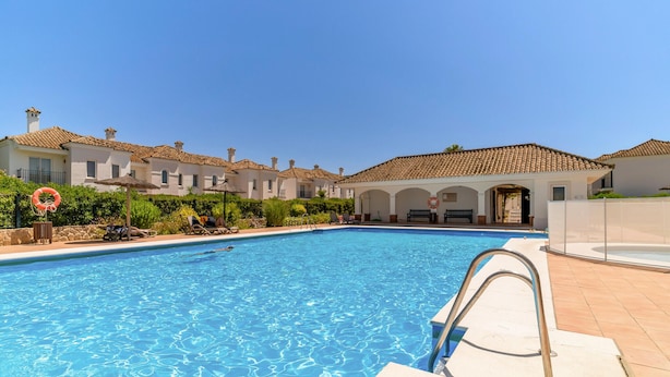 A swimming pool with lounge chairs and umbrellas, surrounded by buildings with tiled roofs. - 2 bedroom nice home in Arcos de la Frontera (Arcos de la Frontera)
