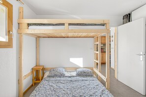 A bunk bed room with a wooden headboard, a bedside table, and a patterned bedspread. - 'Superdevoluy' Apartment with Mountain View and Balcony (Dévoluy)