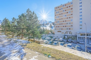 A parking lot with cars, a building with multiple floors, and a mountain in the background.