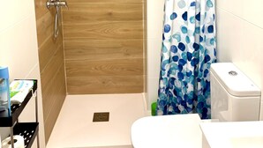 Kylpyhuone, jossa on suihku, wc ja hylly, jossa on hygieniatuotteita.