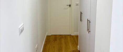 A hallway with a wooden floor, white walls, a white door, and a wardrobe with silver handles.