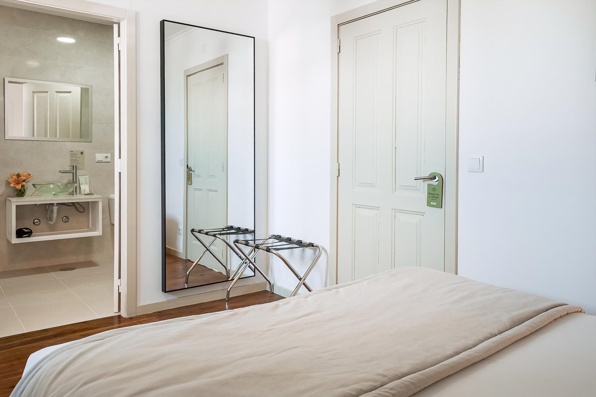 A bedroom with a bed, a mirror, a door, and a bathroom with a sink and mirror.