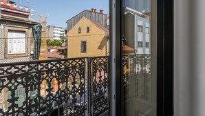 Un balcon orné d’une balustrade en fer forgé, un immeuble jaune coiffé d’un toit à pignon et un ciel d’un bleu limpide.
