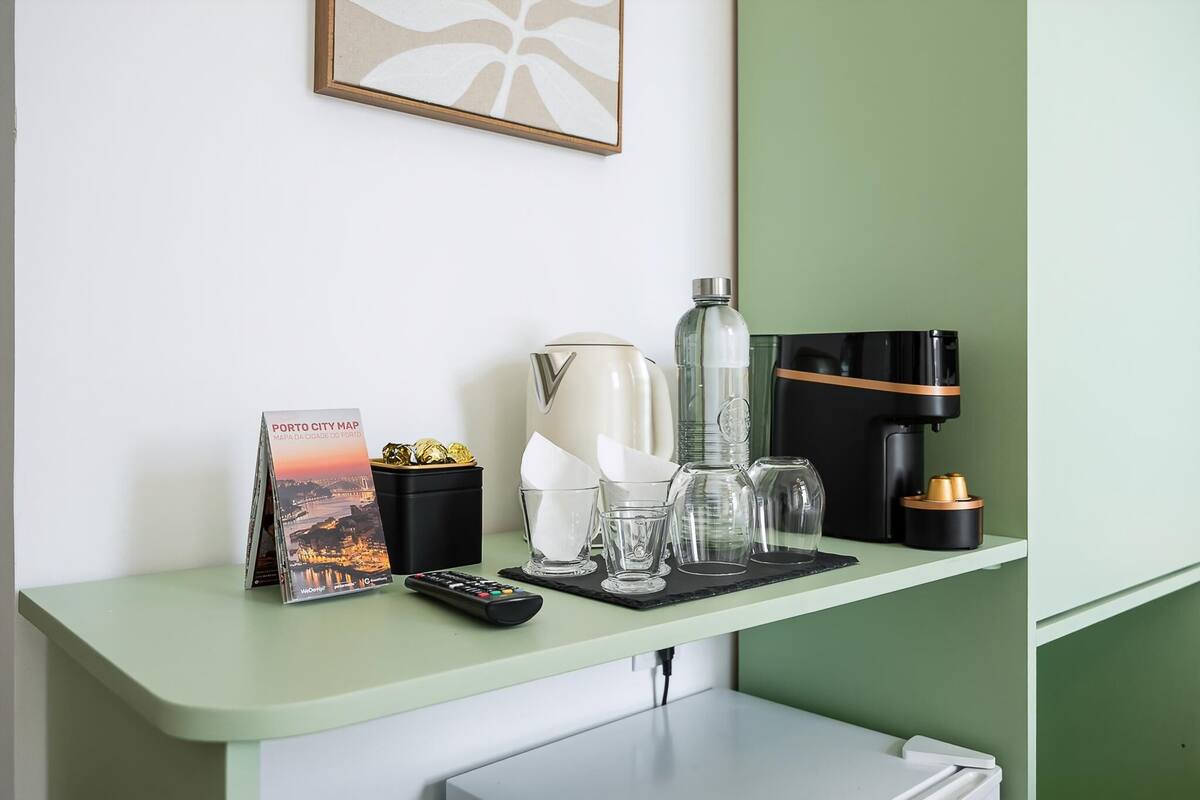 A hotel room counter with a city map, a remote control, a coffee maker, a water bottle, and a coffee machine.