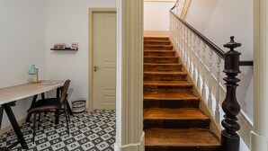 Un escalier avec des marches en bois et des balustrades blanches, un bureau en bois avec une chaise, une petite lampe et un panier posé sur un sol à motifs.