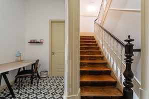 A staircase with wooden steps and white balusters, a wooden desk with a chair, a small lamp, and a basket on a patterned floor. - Guestready - Vanzeleres Collection (Porto)