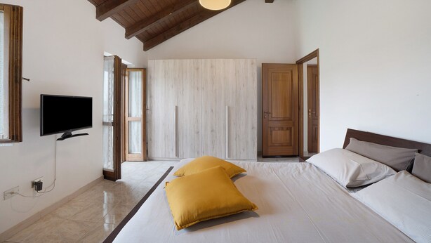 Ein Schlafzimmer mit einem Bett, einem Fernseher, Holzbalkendecken und einer Tür.