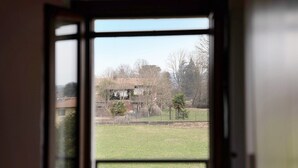 Blick durch ein Fenster mit einem Metallgeländer, ein grasbewachsenes Feld und ein Gebäude im Hintergrund.