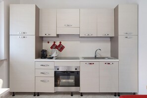 A modern kitchen with white cabinets, a built-in oven, a sink, and a coffee maker.