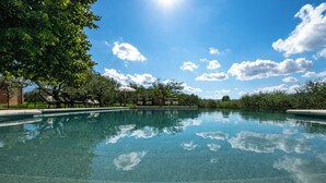 A clear swimming pool with lounge chairs and umbrellas, surrounded by trees and a clear sky. - Podere Gellino 14, Emma Villas (Chianciano Terme)