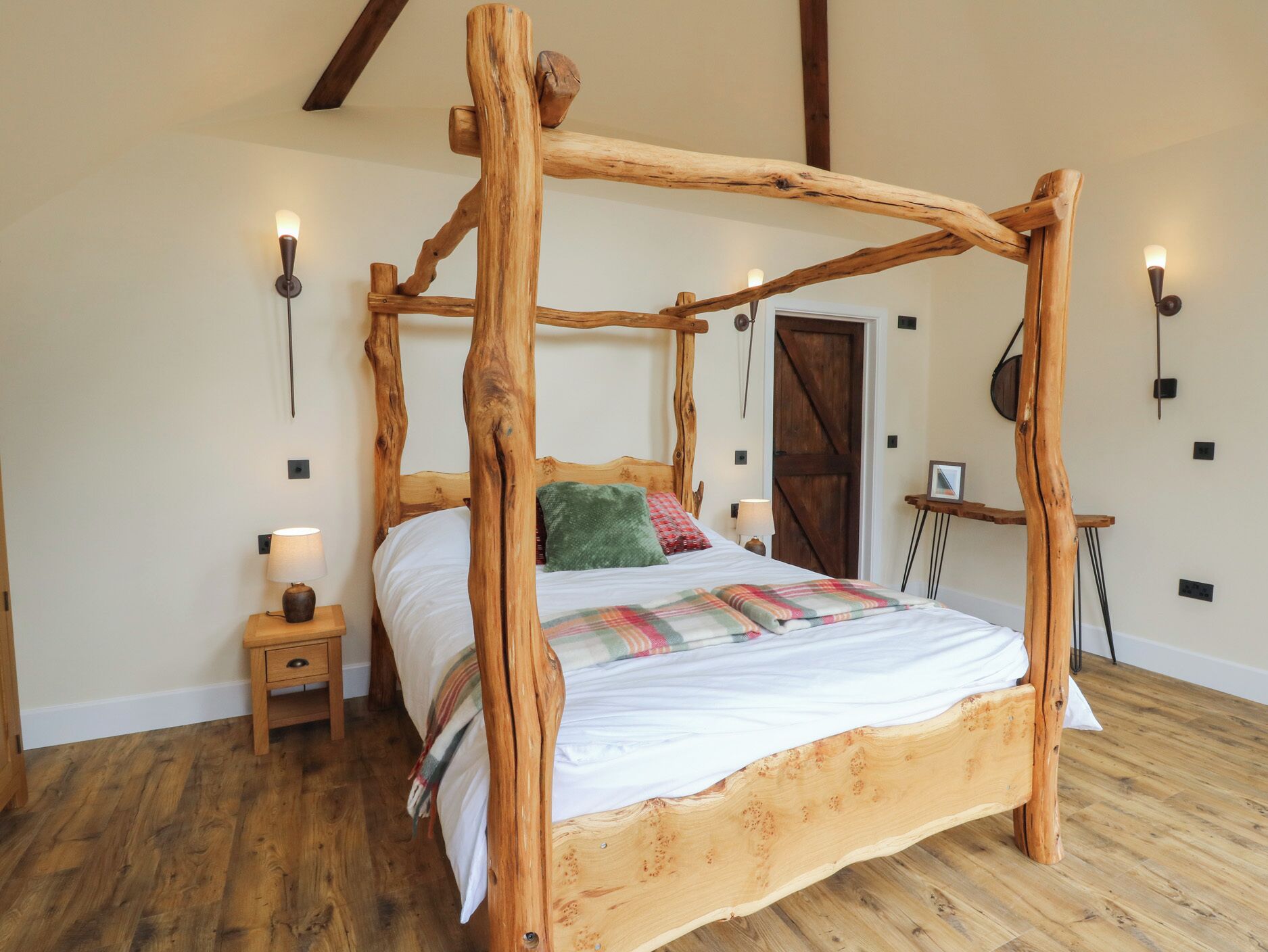 A four-poster bed with a wooden frame, a bedside table with a lamp, and a wooden floor.