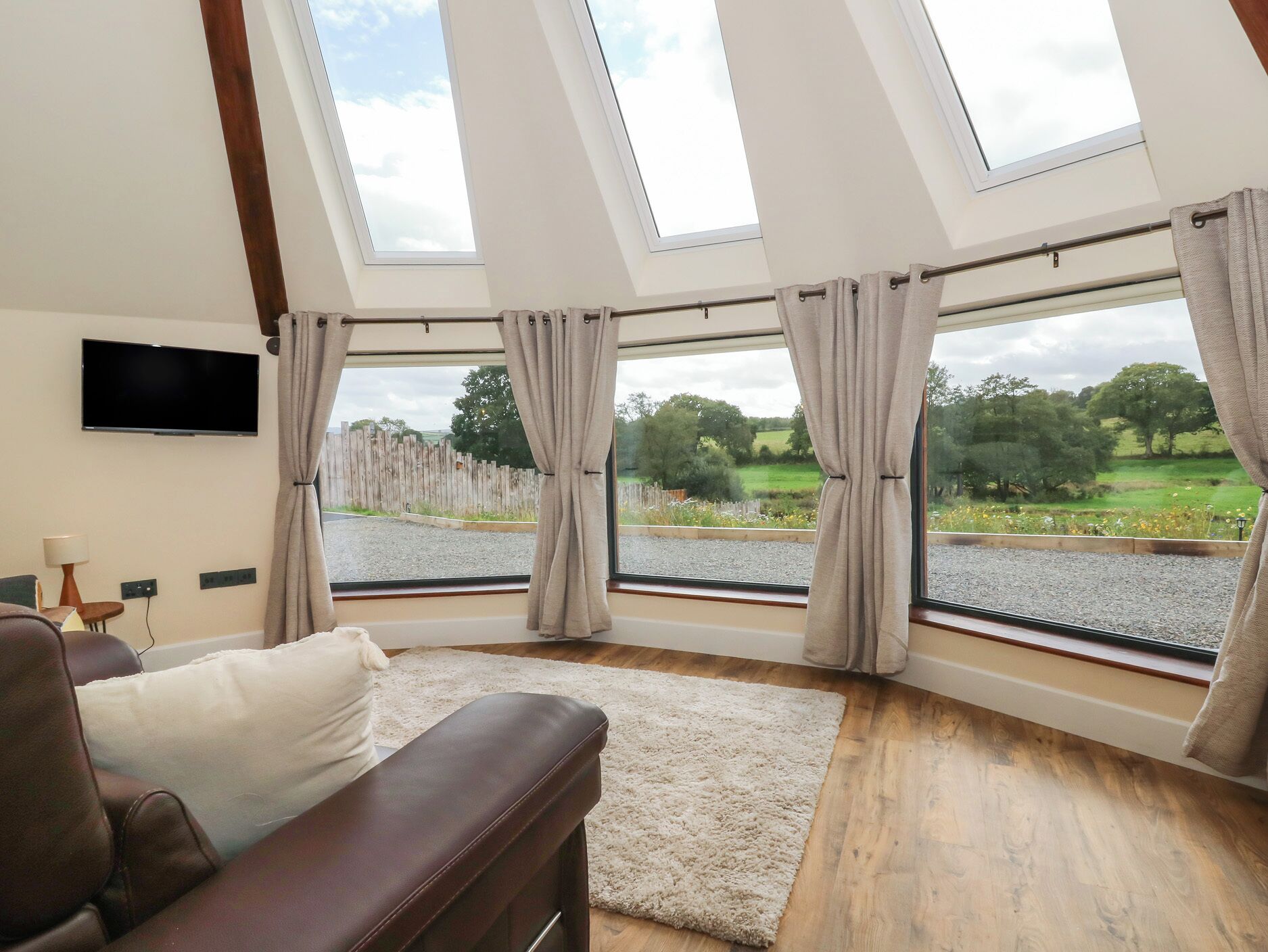A room with a large window, a flat-screen TV, a brown leather sofa, and a white rug.