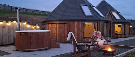 A wooden cabin with a hot tub, a fire pit, and a cozy seating area.
