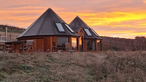 Two wooden cabins with pitched roofs and skylights, surrounded by a grassy field. - Yr Awen - Inspiration (Lampeter)