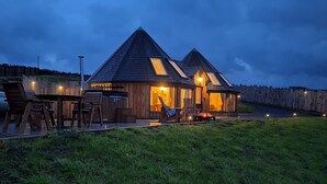 Una cabaña de madera con techo inclinado, un patio con mobiliario exterior y una entrada bien iluminada.