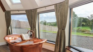 Un baño moderno con una bañera de cobre, ventanas amplias y vistas a una valla de madera y follaje.