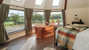 Un dormitorio con un ventanal grande, una bañera de cobre, una cama con manta escocesa y vistas al campo.