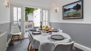 A dining area with a table set for four, a framed picture on the wall, and a view of the outdoors. - Lan Y Mor - Close to Town and Beach (Tenby)