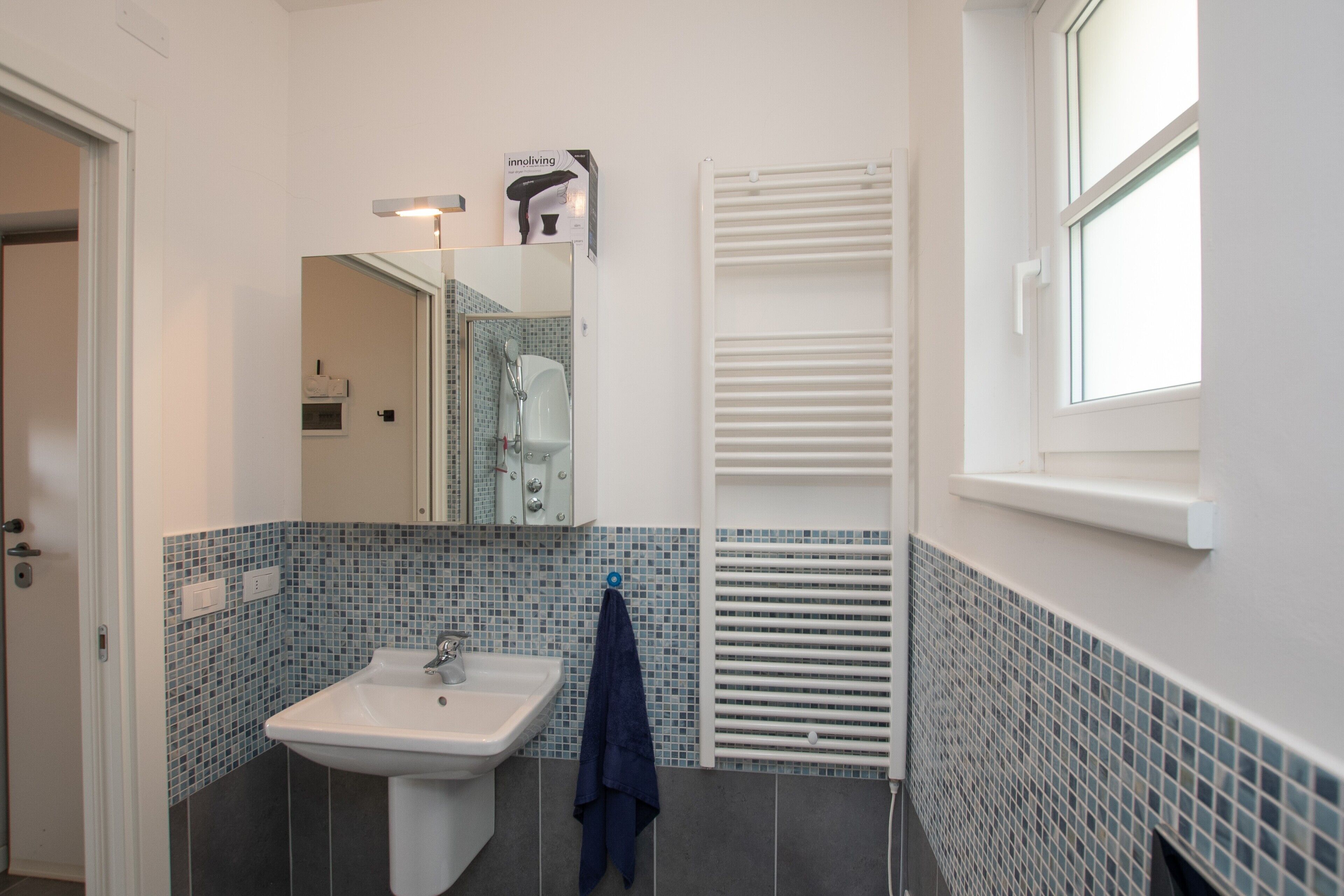 A bathroom with a white sink, a mirror, a towel rack, a window, and a white radiator.