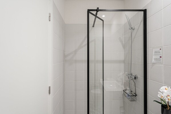 A modern shower with a glass door, a handheld showerhead, and a wall-mounted faucet.
