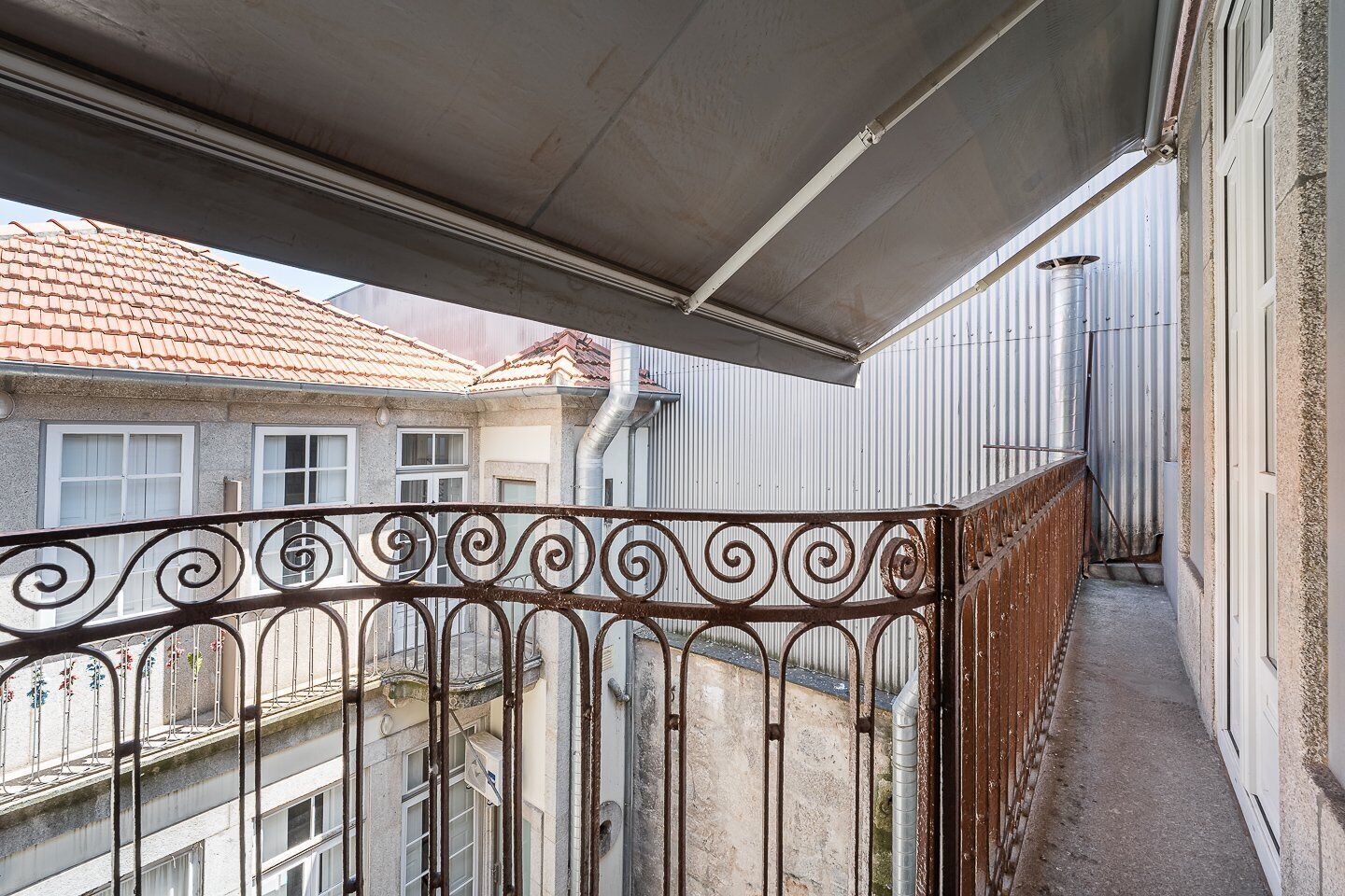 A balcony with a metal railing, a covered area, and a view of adjacent buildings.