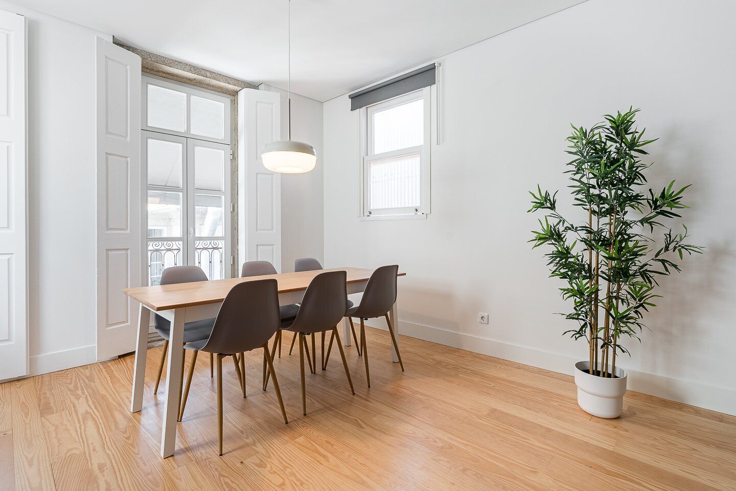 Un coin repas avec une table en bois, six chaises et un plant de bambou en pot.