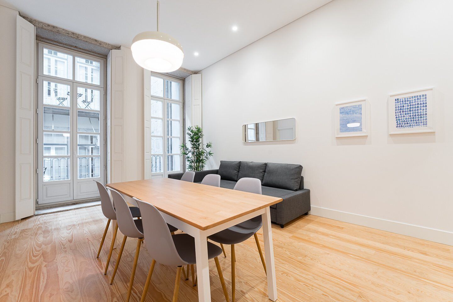 Una sala de estar moderna con una mesa de comedor de madera, un sofá gris y un ventanal con vistas a la ciudad.