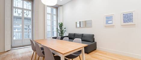 Una sala de estar moderna con una mesa de comedor de madera, un sofá gris y un ventanal con vistas a la ciudad.