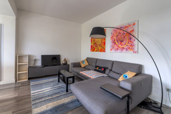 A modern living room with a grey sofa, a flat-screen TV, a coffee table, a floor lamp, and abstract wall art. - Spacious Central Apartment with Wi-Fi and Portable Air Conditioning (Lecce)
