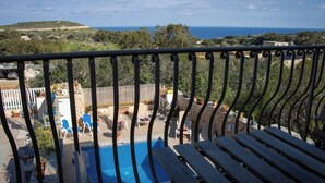 Un balcón con vistas a una piscina, mobiliario exterior y un paisaje distante.