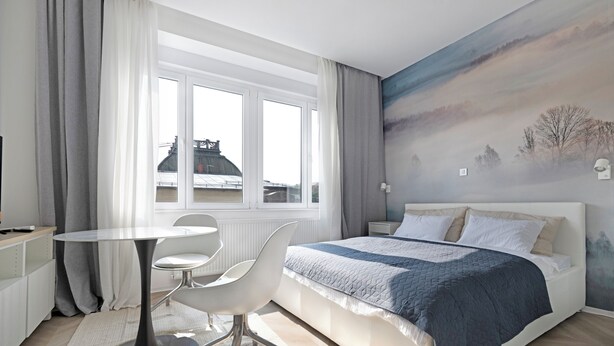 Une chambre moderne avec un grand lit, une table à manger ronde et une vue sur le paysage urbain par la fenêtre.
