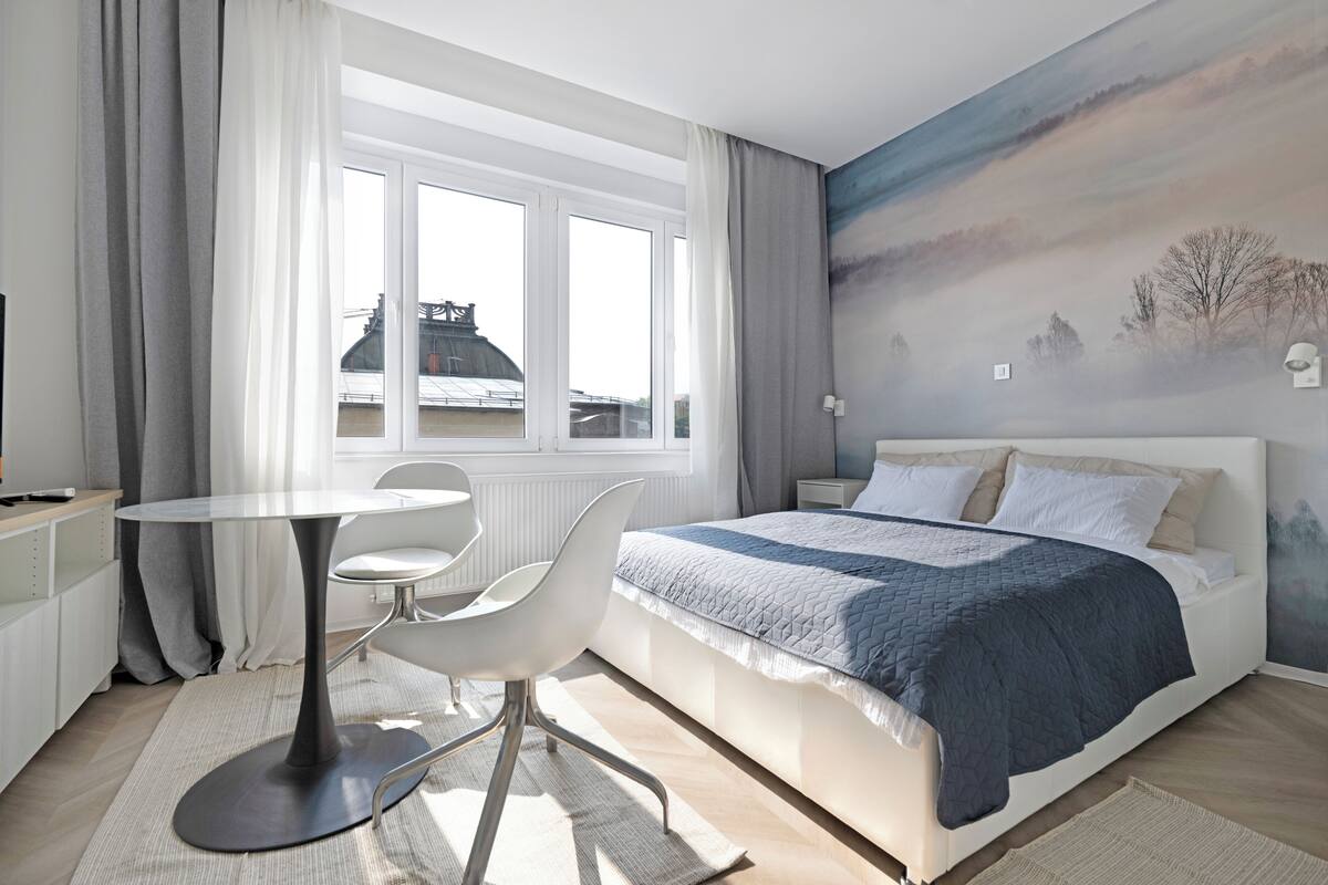 Un dormitorio moderno con una cama grande, una mesa redonda de comedor y vistas a la ciudad desde la ventana.