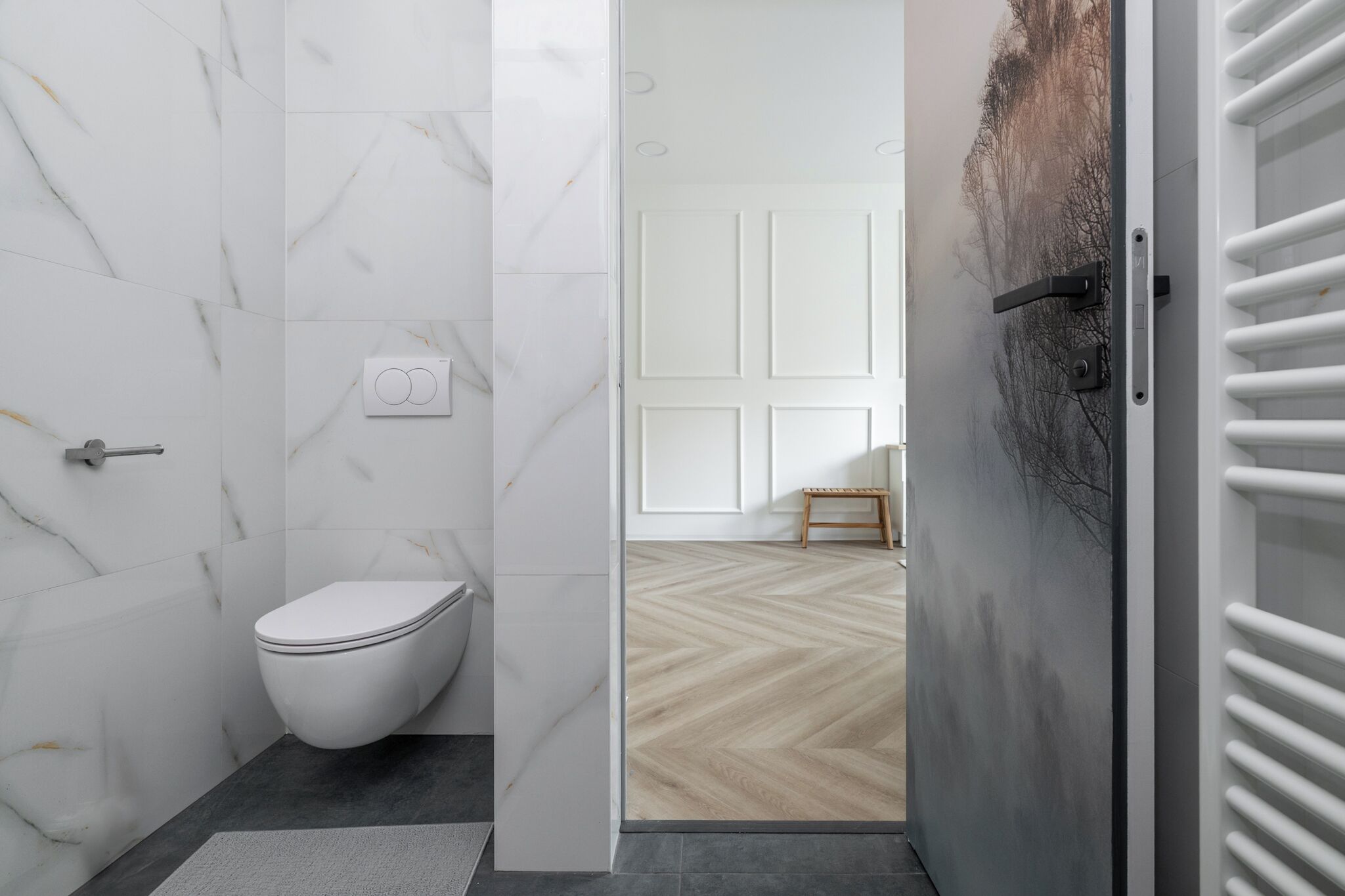A modern bathroom with a white toilet, marble walls, and a wooden floor.