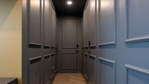 Un couloir étroit aux murs gris et au plancher en bois, qui mène à une porte fermée au bout.