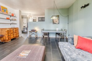 Un saló modern amb un sofà, una taula de centre, una taula de dinar amb cadires, un armari de fusta i una cuina al fons.
