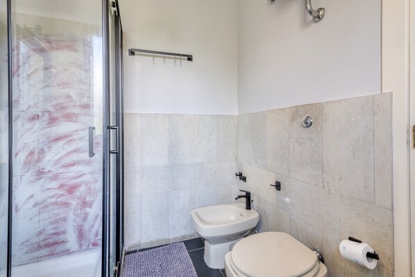 A bathroom with a glass shower enclosure, a bidet, and a toilet.