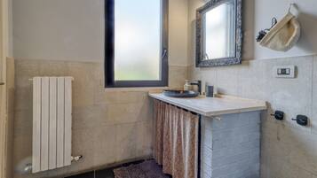 A bathroom with a window, a towel rack, a sink, a mirror, and a towel hanging on the wall.