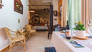 A cozy room with wicker chairs, a dining table with a wine bottle, a large wheel, and a rustic stone wall. - Gîte La Grange de Soyons (Soyons)