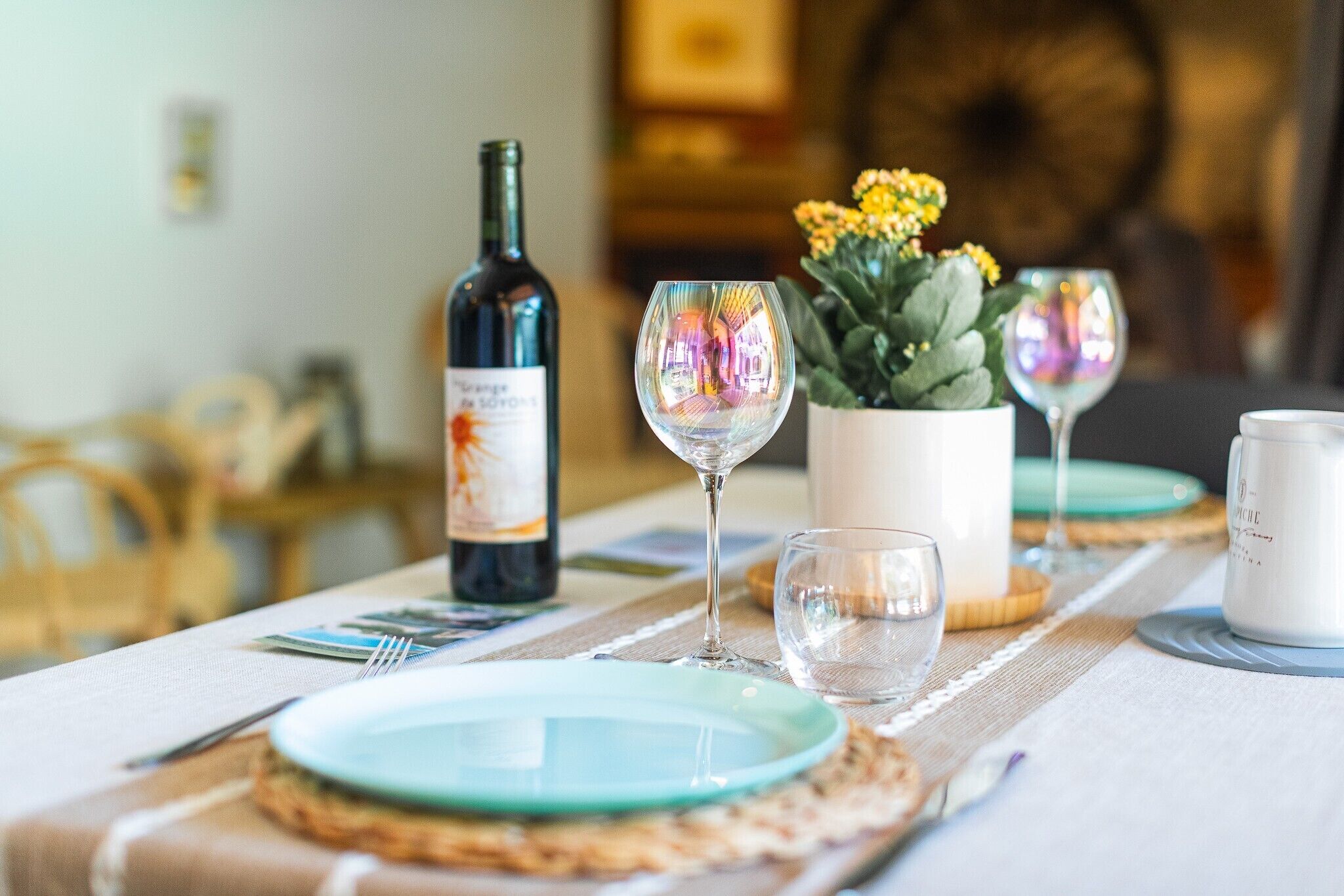 Una mesa de comedor dispuesta con platos, copas de vino, una botella de vino y un florero con flores.