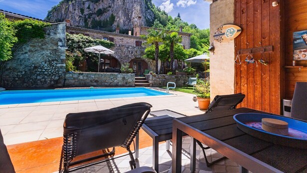 A pool area with stone walls, a wooden door, and outdoor furniture. - Gîte La Grange de Soyons (Soyons)