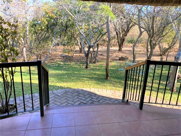 A covered outdoor area with a herringbone-patterned floor, metal railings, and a view of a grassy landscape with trees. - Double Lodge in Natural African Bush - 2111 (Bulawayo)