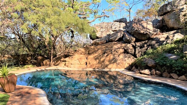 A swimming pool with clear water, surrounded by rocks and trees. - Double Lodge in Natural African Bush - 2111 (Bulawayo)