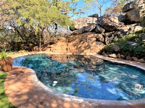 A swimming pool with clear water, surrounded by rocks and trees. - Double Lodge in Natural African Bush - 2111 (Bulawayo)