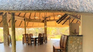 A covered outdoor dining area with a thatched roof, stone walls, and a stone counter with a mirror. - Double Lodge in Natural African Bush - 2111 (Bulawayo)