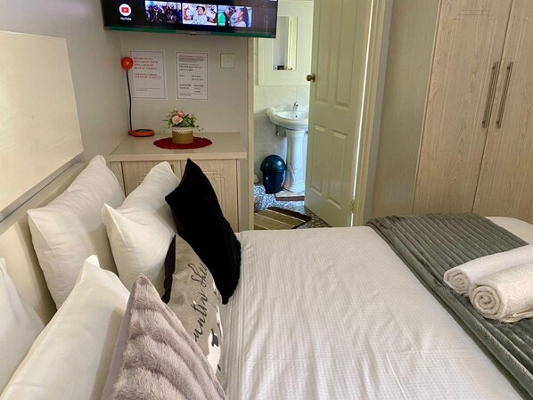 A hotel room with a bed, pillows, a TV mounted on the wall, a small table with a vase, and a door leading to a bathroom. - Studio Near Airport City Centre - 2317 (Harare)