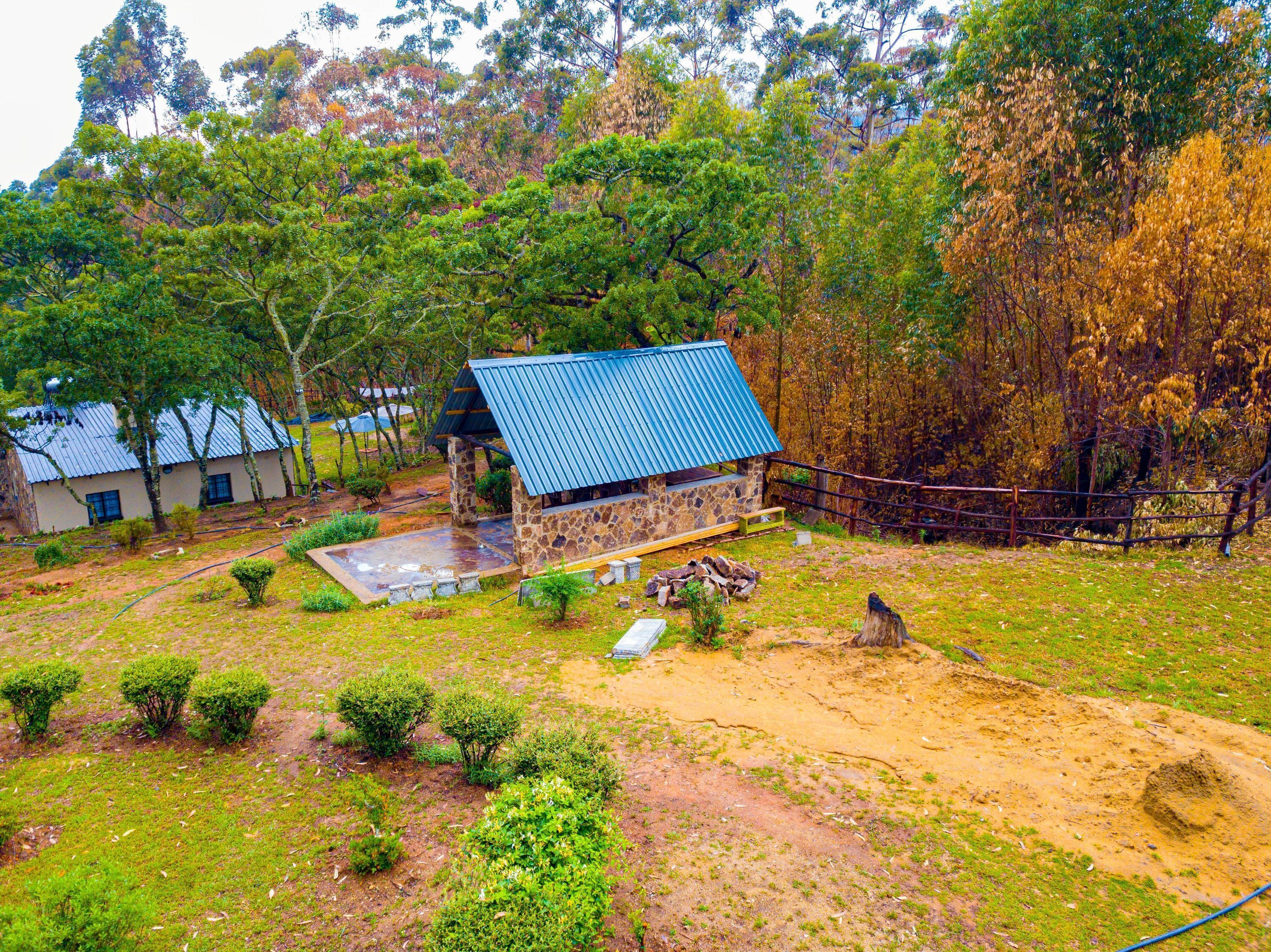A stone building with a blue roof, surrounded by a fenced yard with a small pond and various shrubs.